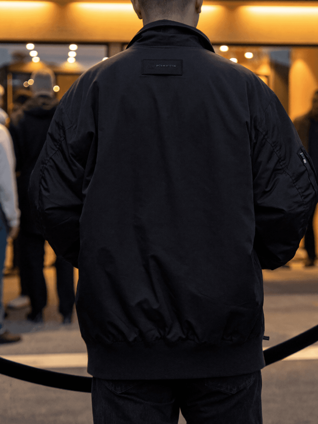 A door supervisor at the rope of a busy venue at dusk